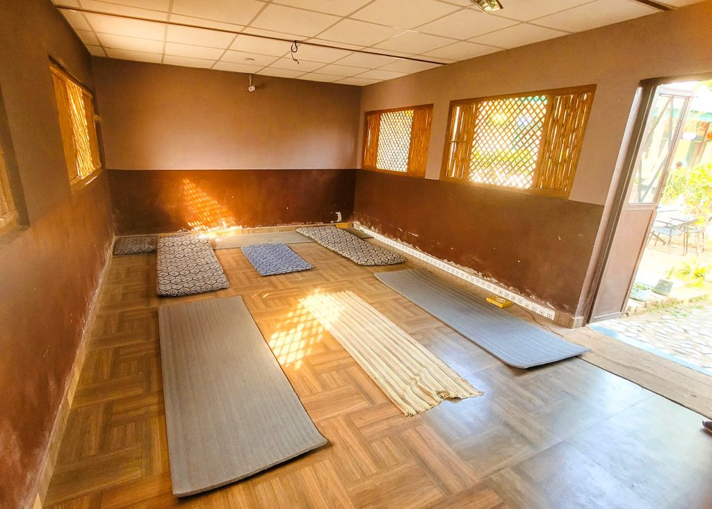 Inner sanctum of serenity: Inside the yoga hall at Sage House Yoga's retreat center, a spacious and tranquil space awaits, adorned with natural light streaming through large windows, creating a harmonious and uplifting environment for yoga practice and self-reflection.