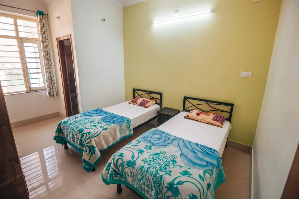 Comfort and serenity in Rishikesh: Cozy rooms at Sage House Yoga provide a peaceful retreat, featuring relaxing decor, comfortable furnishings, and a tranquil ambiance for a rejuvenating stay.