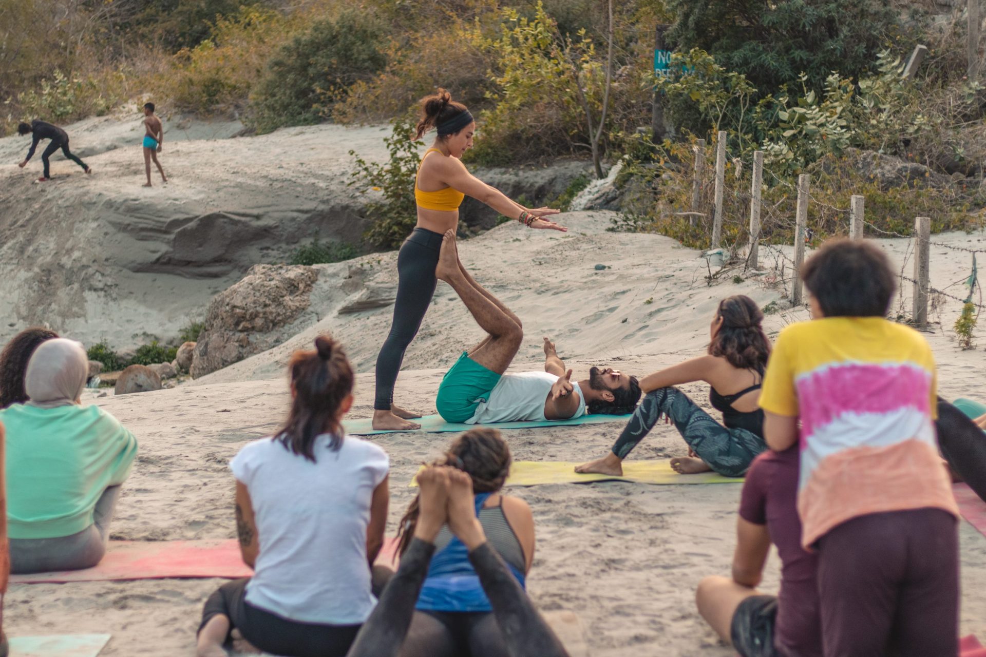Flowing grace by the beach: In the scenic beauty of Rishikesh, students at Sage House Yoga engage in beach Acro Yoga, showcasing their versatility and skill as they perform a variety of poses, creating a dynamic and captivating display of strength and flexibility.