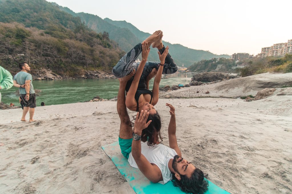 Playful serenity by the beach: In Rishikesh, Sage House Yoga offers a delightful session of beach Acro Yoga, where participants gracefully balance and flow, creating a harmonious and joyful atmosphere.
